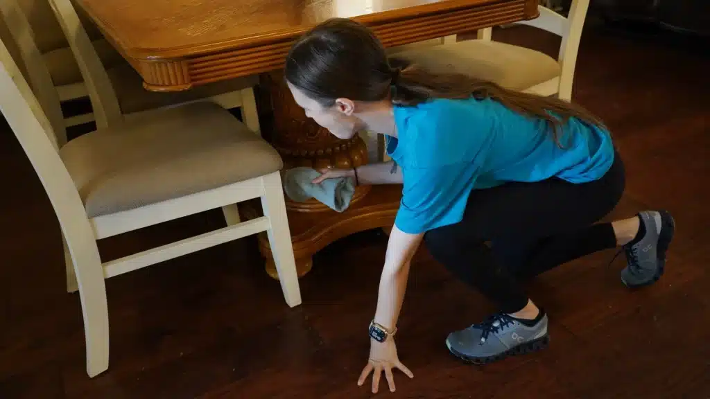 Woman cleaning under a dining table with a cloth, showcasing professional house cleaning services in a residential setting.