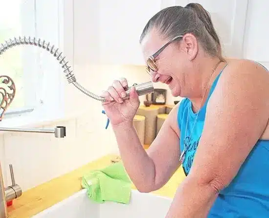 Woman laughing while using a kitchen faucet sprayer, showcasing a lighthearted moment during cleaning.