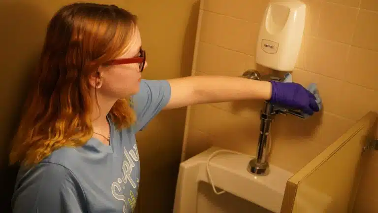 Simply Maid Sparkle Technician wiping a soap dispenser and wall in purple gloves